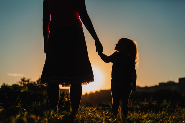 silhouette de mère et fille tenant la main au coucher du soleil - Photo, image
