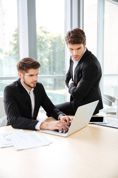 Два бізнесмени використовують ноутбук в офісі разом
 - Фото, зображення
