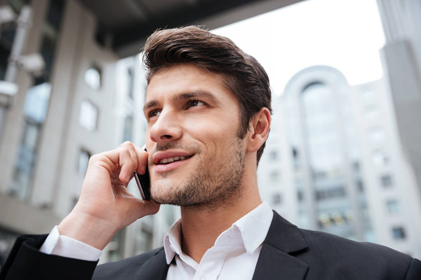 Cheerful attractive young businessman talking on cell phone outdoors - Fotó, kép