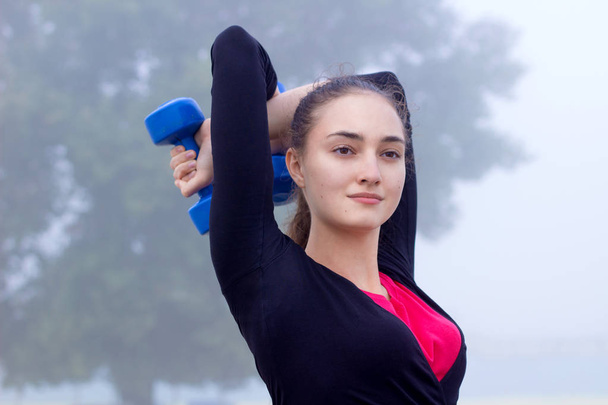 Молодая спортсменка, занимающаяся с гантелями во время тренировки ворко
 - Фото, изображение