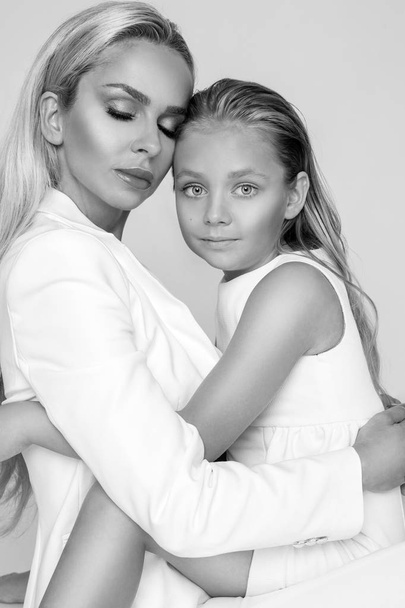 Beautiful woman mother with daughter snuggling together and show love, smartly dressed in a white dress - Foto, afbeelding
