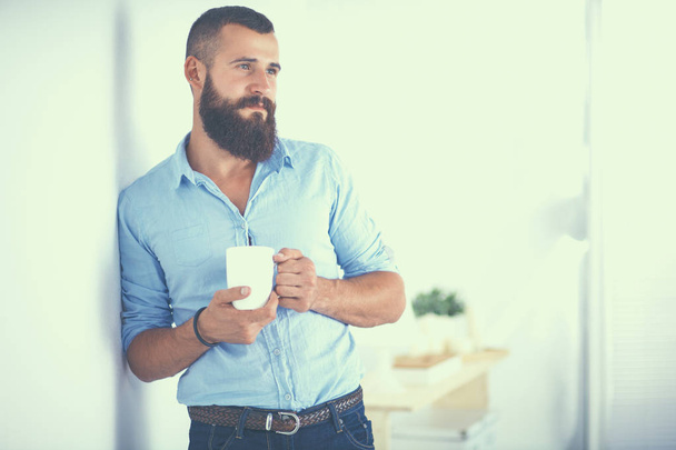 Young man standing near wall and holding cup of coffee - Foto, immagini