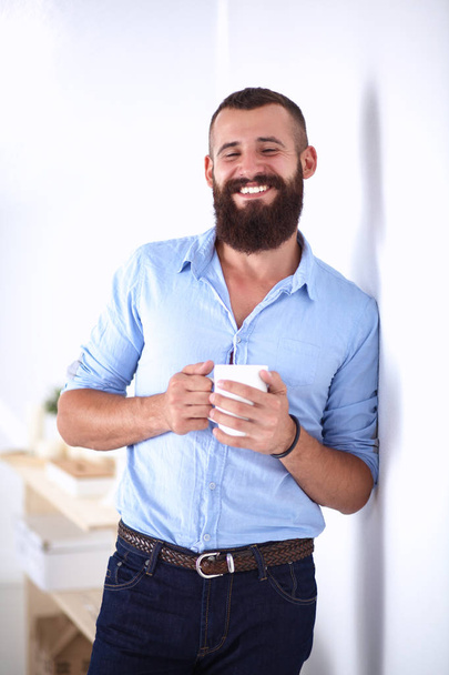 Young man standing near wall and holding cup of coffee - Fotoğraf, Görsel