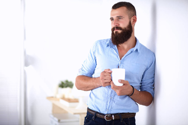 Young man standing near wall and holding cup of coffee - Φωτογραφία, εικόνα