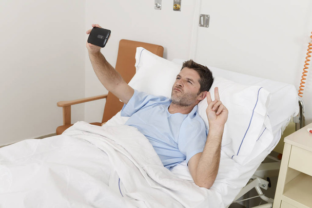 attrayant homme couché sur lit hôpital clinique tenant téléphone mobile prenant autoportrait selfie photo
 - Photo, image