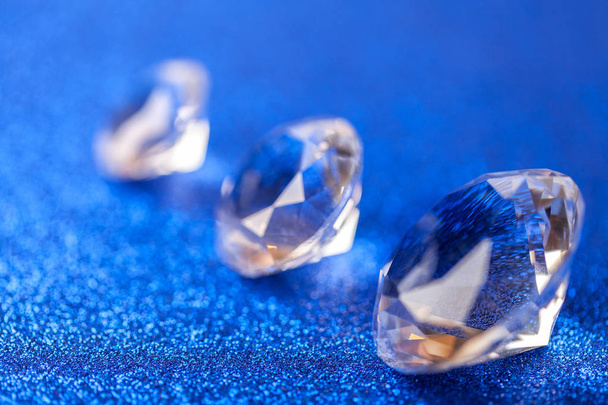 Three grand expensive diamonds laid on the diagonal on blue sparkling sequins background, macro . Big brilliant closeup. - Photo, Image