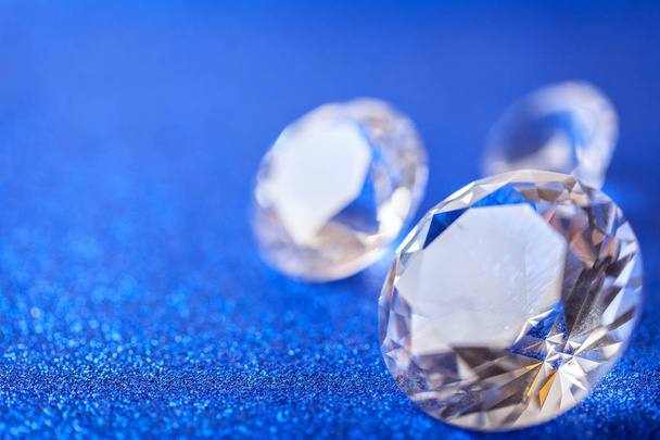 Large expensive diamonds laid on blue sparkling sequins background, macro . Big brilliant closeup. - Photo, Image