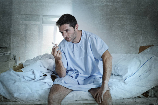 aantrekkelijke jongeman op zoek triest en ongerust bij ziekenhuis bed smo - Foto, afbeelding