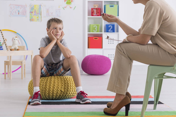 Boy sitting on a pouf, talking with a psychotherapist - Фото, изображение