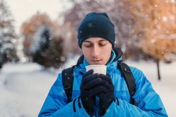 Portrait of a man wearing bright blue winter sporty jacket and holding hot drink in disposable takeaway paper cup, outdoor shot - Foto, Imagem
