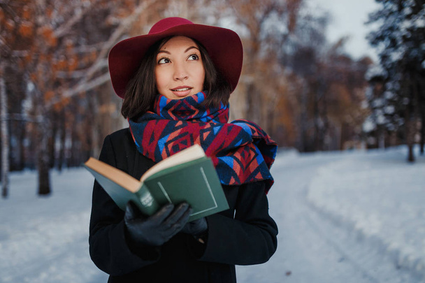 Giovane donna con cappello rosso che tiene e legge libro di poesia in sfondo foresta invernale
 - Foto, immagini