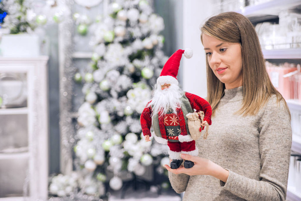 Pretty girl holding Santa Clause plush toy. Smiling woman holding small Santa Claus. Father Christmas toy in girl's hands. Holiday season and Christmas concept - Photo, image