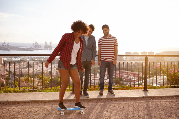 Young men watching girl skateboarding - Фото, изображение