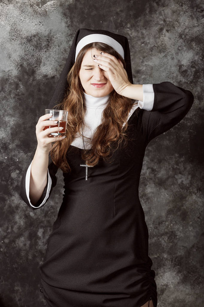 nun holding a glass with alcohol on a dark background.woman leaning against his head arm. - Foto, Bild