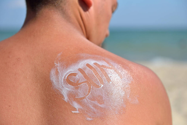 The word sun written with sun cream on the back of a  young man  - Foto, Bild