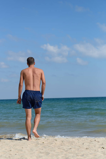 Young man with athletic body in blue shorts is walking true the  - Φωτογραφία, εικόνα