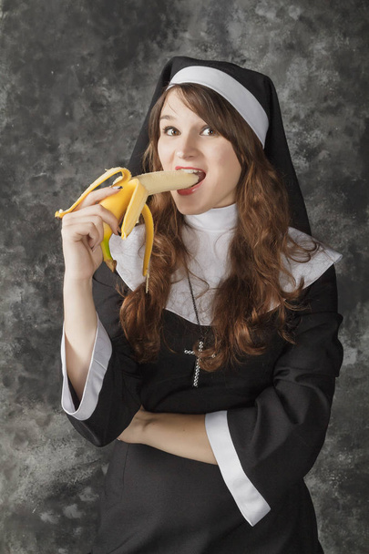 καλόγρια, κρατώντας μια μπανάνα και δαγκώνει τον σε σκούρο φόντο - Φωτογραφία, εικόνα