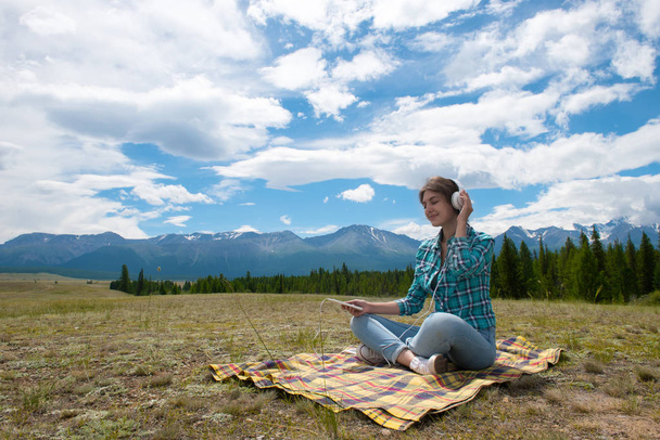 Woman in headphones listening music in a field and at the mountain. - 写真・画像