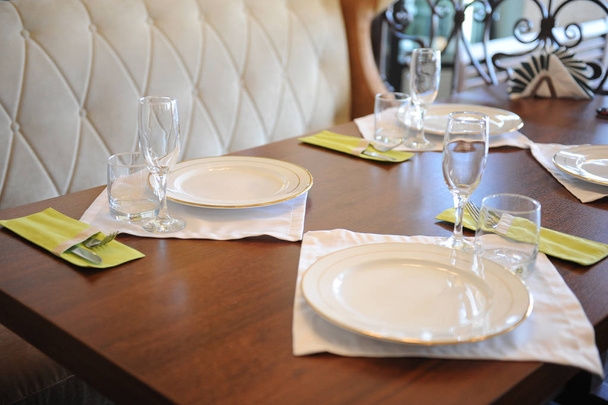 Обдарований стіл у ресторані. Білі тарілки, окуляри на білій тканині на дерев'яній поверхні
 - Фото, зображення