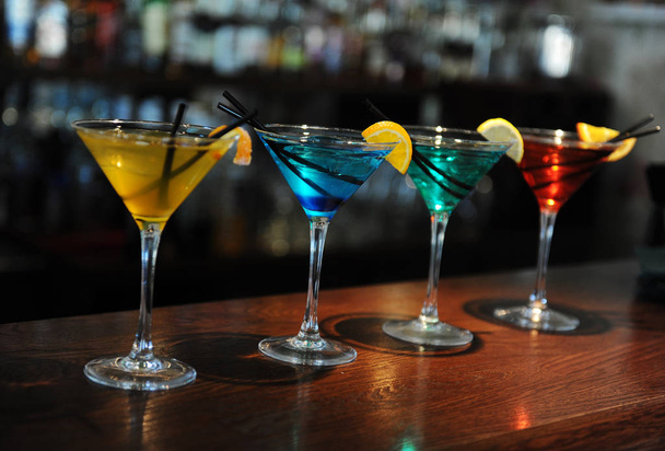 Vier gekleurde cocktails op de bar. Geel, blauw, groen, rood. Ingericht met een schijfje citroen - Foto, afbeelding