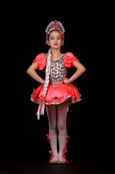 Cute little girl wearing native russian costume isolated on black background. She is dancing. - Photo, image