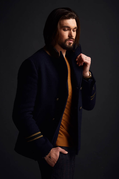 Handsome stylish man with long hair in dark studio wearing blue jacket - Photo, Image