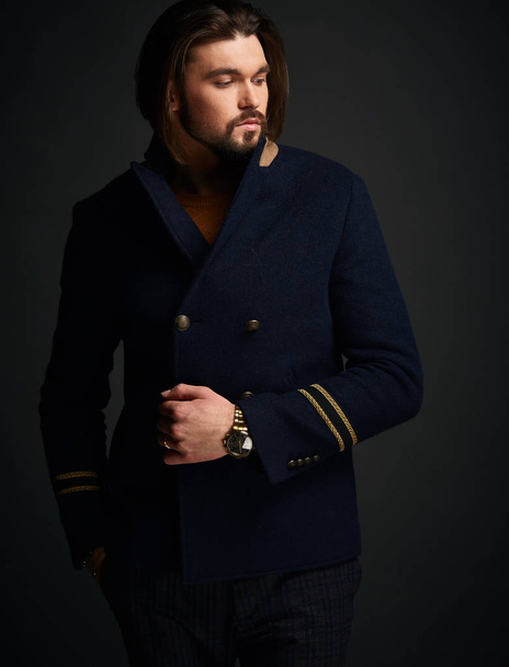 Attractive stylish man with long hair in dark studio wearing classic blue jacket - Foto, afbeelding