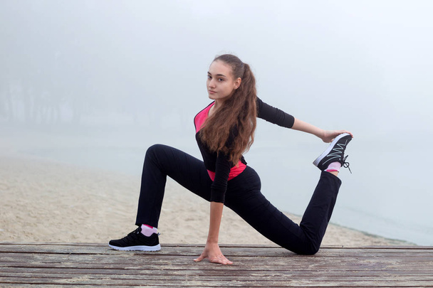 Молодая спортивная девушка растягивается во время фитнес-тренировки на открытом воздухе
 - Фото, изображение
