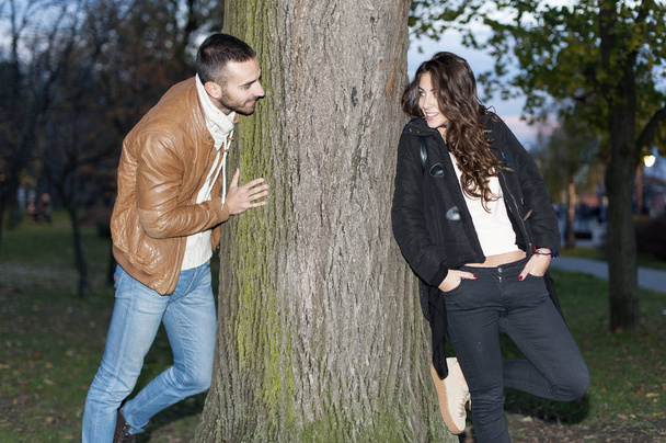 Young couple in love are chasing around a tree - Foto, afbeelding
