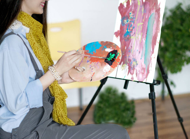 Jeune peintre souriante peignant dans son atelier
. - Photo, image