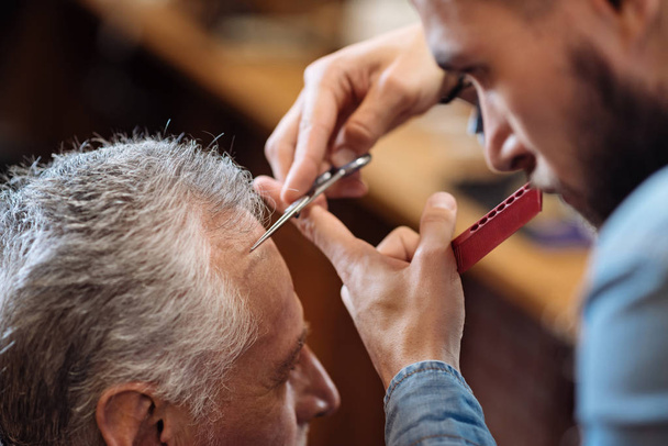 Hair dresser cutting bang of senior man - Фото, зображення
