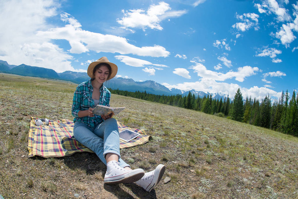 Young woman reading book and sitting in a field. Mountains background. - Фото, зображення