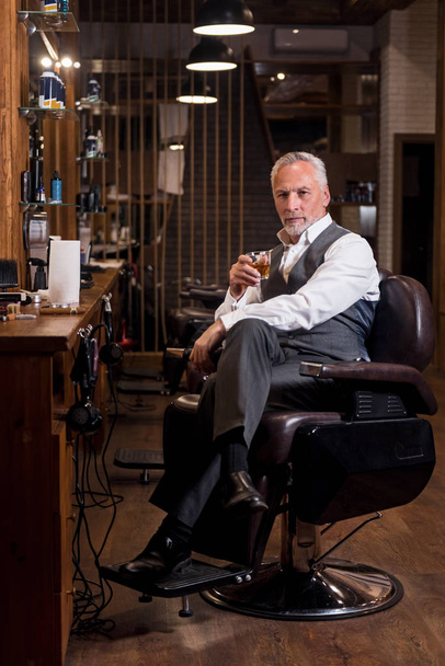 Elegant senior man with whiskey glass and cigar at barbershop - 写真・画像