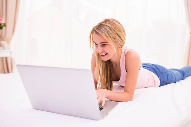 Cheerful attractive young woman lying on bed and using laptop - Zdjęcie, obraz