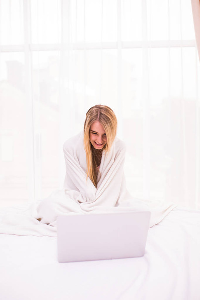 Atractiva mujer joven acostada en la cama bajo la cubierta y utilizando el ordenador portátil
 - Foto, Imagen