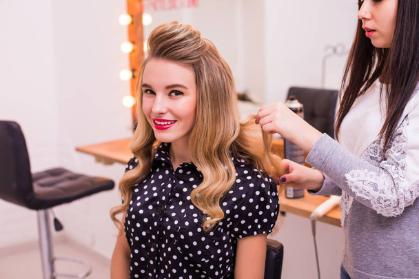 Female hairdresser standing and making hairstyle to cute lovely young woman in beauty salon - 写真・画像
