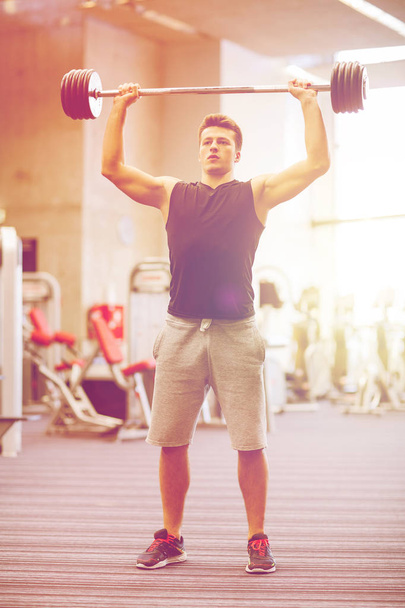 young man flexing muscles with barbell in gym - Foto, Imagen