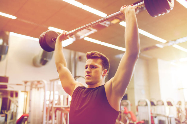 young man flexing muscles with barbell in gym - Fotoğraf, Görsel