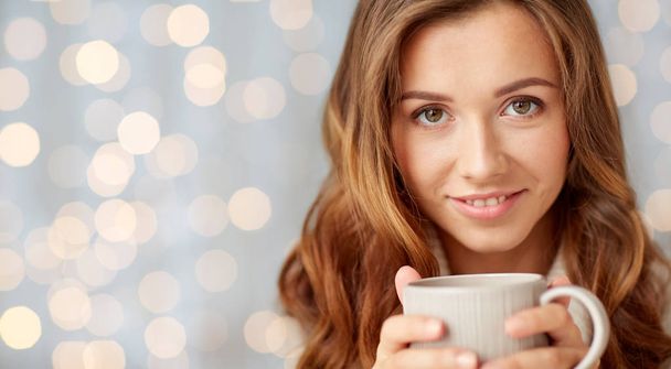 close up of happy woman with tea cup over lights - Foto, Imagen