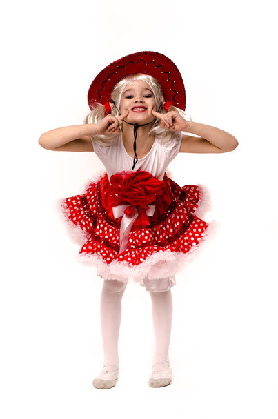 Cute little caucasian girl wearing red skirt, t-shirt with flowers and cowboy hat isolated on white background. She is dancing. - Fotografie, Obrázek