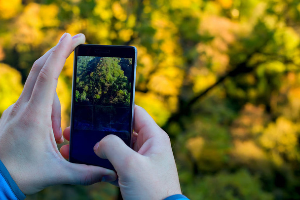 Black phone in man's hands making photo of autumn landscape - Foto, Imagen