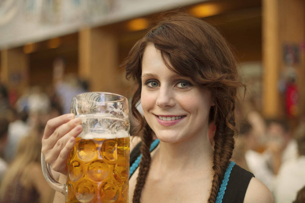  German woman wearing traditional dirndl and holding a beer mug at Oktoberfest - Фото, изображение