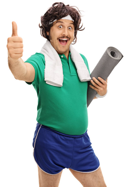 Retro sportsman holding an exercising mat and giving a thumb up - Foto, imagen