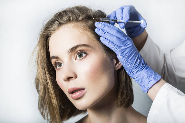 Doctor aesthetician makes head beauty injections to beautiful female patient - 写真・画像