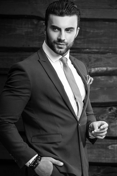 Schwarz-weißes Porträt eines schönen modischen Mannes im eleganten Anzug vor Holzhintergrund. - Foto, Bild