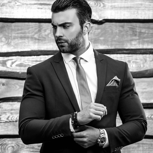 Μαύρο-άσπρο πορτρέτο του όμορφη μοντέρνα άνθρωπος με κομψό κοστούμι ξύλινο υπόβαθρο. - Φωτογραφία, εικόνα