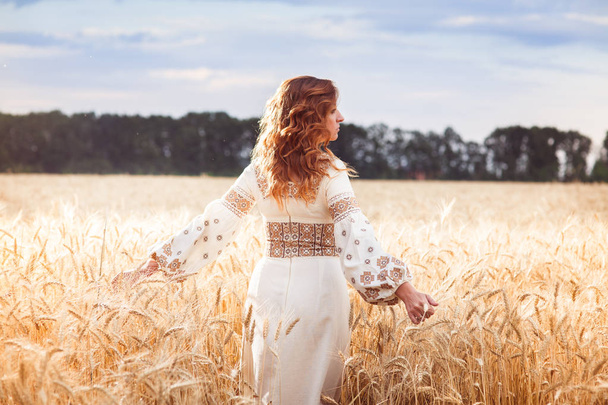 Mooie vrouw gekleed in geborduurde blouse in tarweveld - Foto, afbeelding