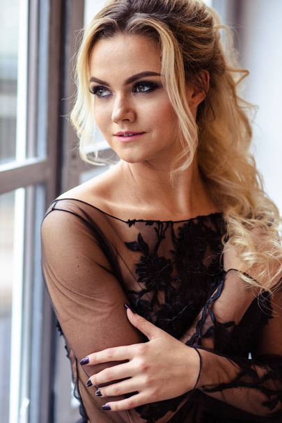 Beautiful young woman in gorgeous black evening dress with perfect makeup and hair style - Foto, imagen