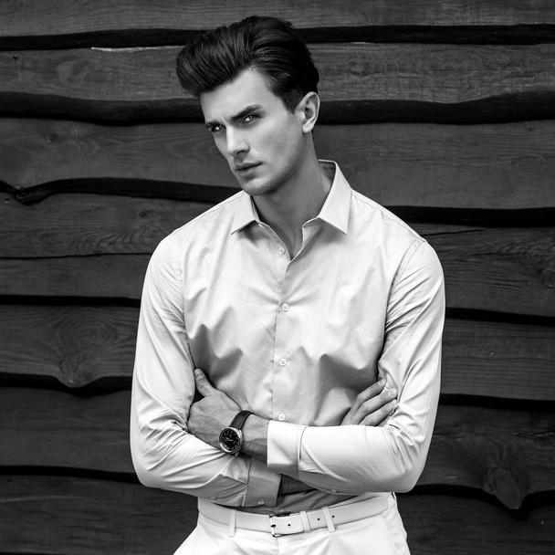 Black-white portrait of young handsome fashionable man in white suit against wooden wall - Photo, image