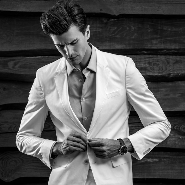 Black-white portrait of young handsome fashionable man in white suit against wooden wall - Φωτογραφία, εικόνα